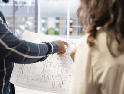 Real estate expert presenting office space layout to woman using blueprints and architectural plans, evaluating the property for potential startup relocation and investment. Modern workspace.